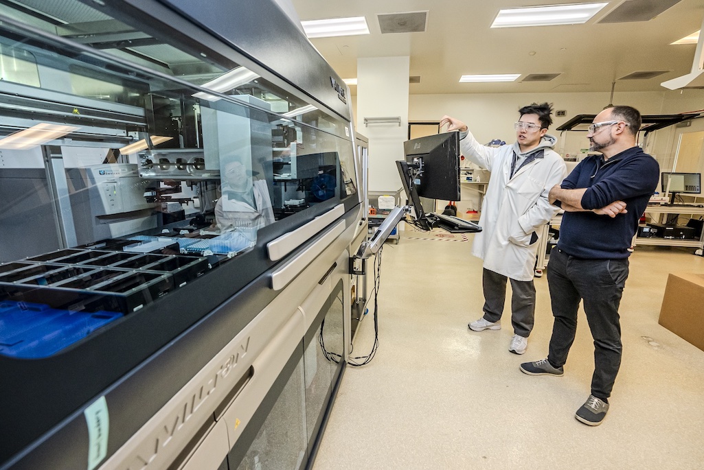 <p>Staff Scientist Hector Garcia Martin (right) and Automation Engineer Randy Louie discuss a liquid handling robot at JBEI.</p>
