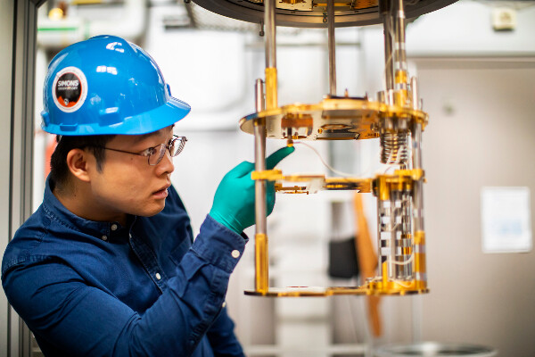 a person in a hardhat inspecting a metal device with gold plates and wires