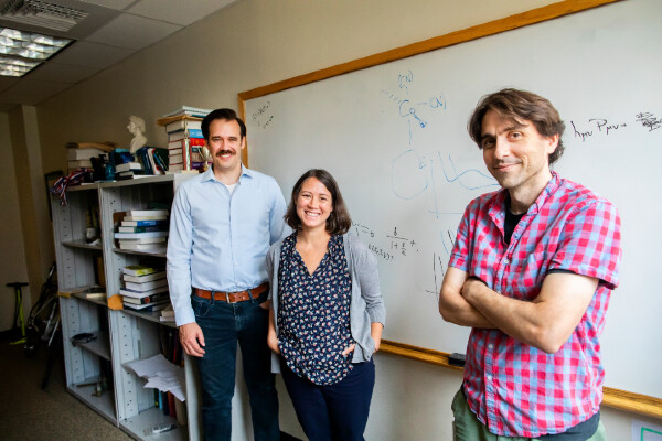 three people in front of a white board with equations and chemical formulas