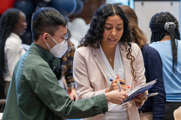 Two students look together at a notebook amid a larger group