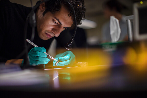 Mohsen Azadi wears latex gloves and wields a scalpel while preparing a photophoretic levitation experiment.