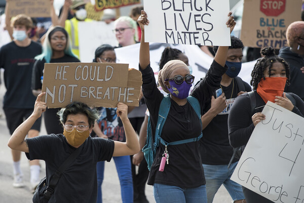 Masked people in a protest crowd holding signs that read Black Lives Matter, He Could Not Breathe, and Justice 4 George Floyd.