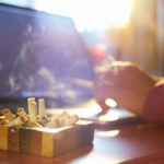 <p>Close up of ashtray full of cigarette, with man in background working on laptop computer and smoking indoors on early morning. Concept of addiction and abuse of nicotine.</p>
