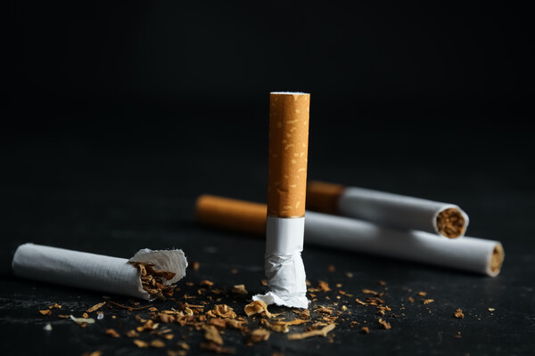 A put-out cigarette standing on its end, next to half of another crumpled cigarette. In the background are two whole cigarettes.